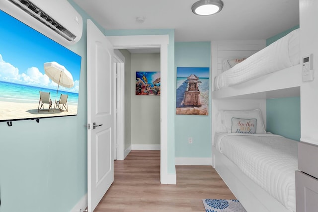 bedroom with baseboards, light wood-style flooring, and a wall unit AC