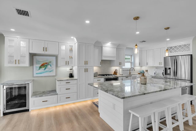 kitchen with white cabinets, wine cooler, a kitchen breakfast bar, a sink, and visible vents