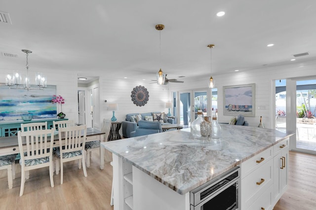 kitchen featuring open shelves, open floor plan, light wood-style floors, stainless steel microwave, and white cabinetry