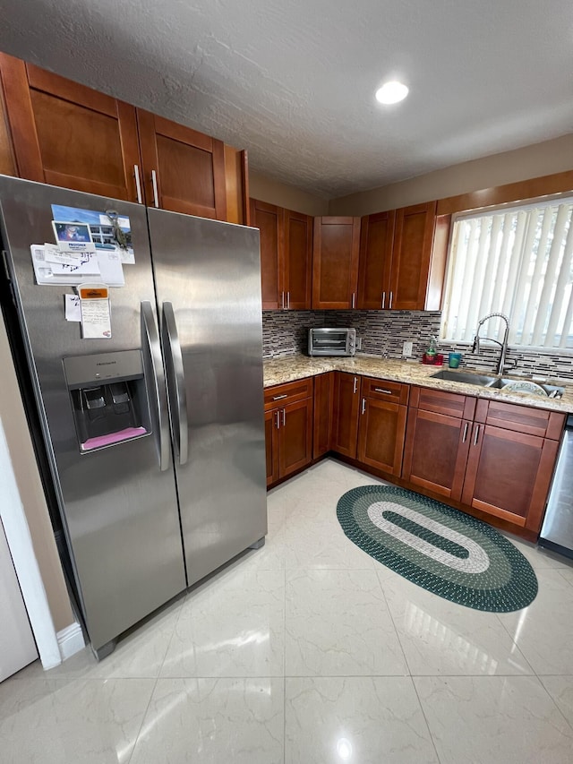 kitchen with tasteful backsplash, sink, light stone countertops, and appliances with stainless steel finishes