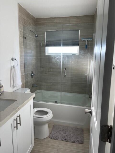 full bathroom with combined bath / shower with glass door, vanity, and toilet