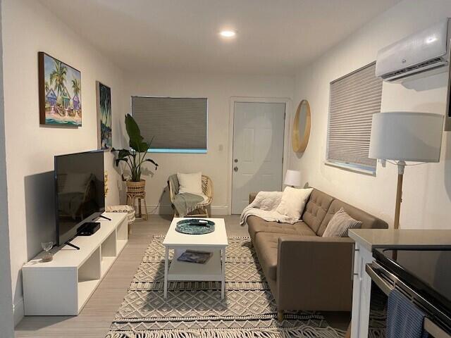 living area featuring light wood-style floors, recessed lighting, a wall unit AC, and baseboards