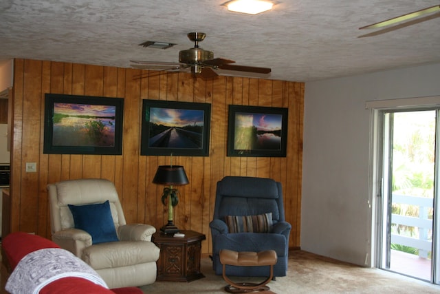 sitting room featuring ceiling fan, wooden walls, light colored carpet, and a textured ceiling