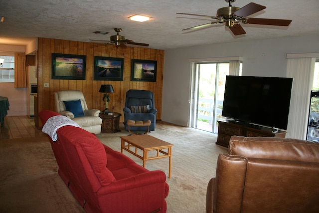 carpeted living room with ceiling fan, a textured ceiling, and wood walls