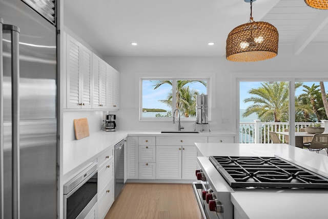 kitchen featuring appliances with stainless steel finishes, pendant lighting, white cabinetry, sink, and light wood-type flooring