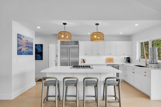 kitchen with light wood finished floors, appliances with stainless steel finishes, a kitchen breakfast bar, light countertops, and a sink