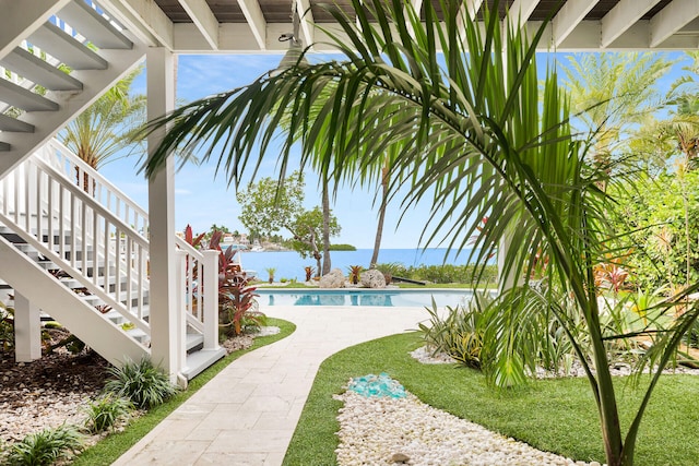 outdoor pool with a water view, stairway, and a yard