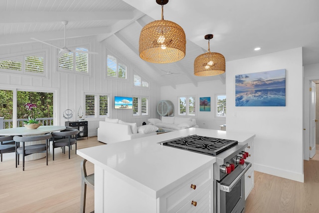 kitchen featuring high end stainless steel range, light hardwood / wood-style floors, white cabinets, a kitchen island, and decorative light fixtures