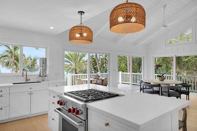 kitchen featuring sink, white cabinetry, lofted ceiling with beams, high end stove, and decorative light fixtures