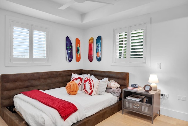 bedroom with multiple windows, hardwood / wood-style floors, ceiling fan, and a tray ceiling