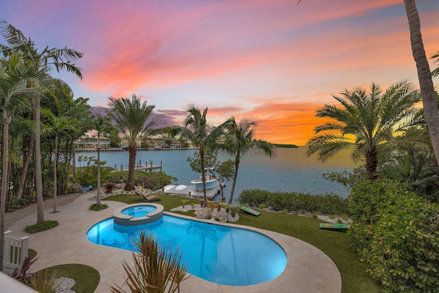 pool at dusk with an in ground hot tub, a water view, and a patio