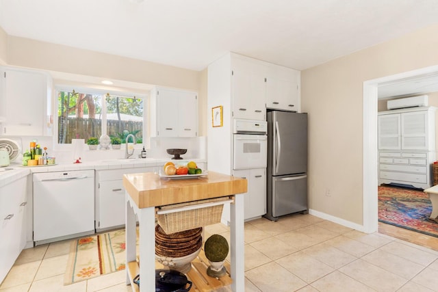 kitchen with white cabinetry, sink, a wall mounted air conditioner, and white appliances