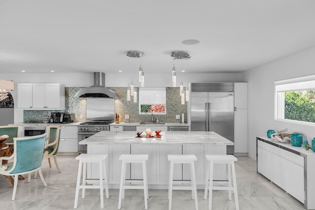 kitchen with sink, premium appliances, a kitchen island, pendant lighting, and wall chimney range hood