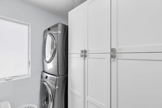 clothes washing area with cabinets and stacked washer / dryer