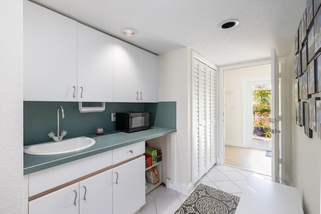 kitchen featuring a sink, light tile patterned flooring, a textured ceiling, black microwave, and white cabinets
