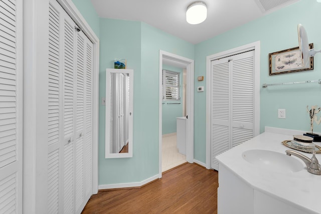 bathroom with a closet, wood finished floors, baseboards, and vanity