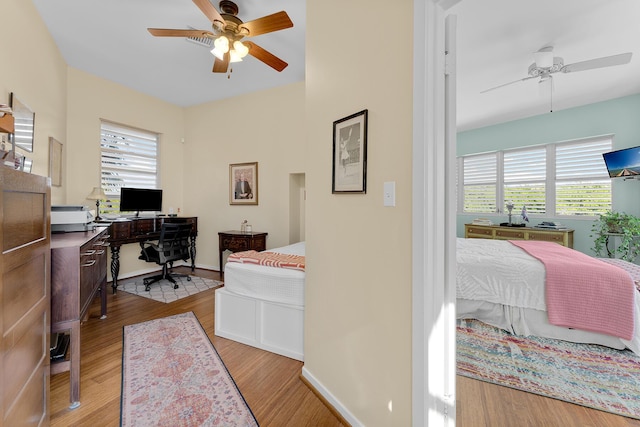 bedroom with wood finished floors, multiple windows, a desk, and ceiling fan