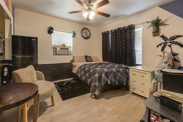 bedroom featuring multiple windows, black fridge, cooling unit, and light hardwood / wood-style floors