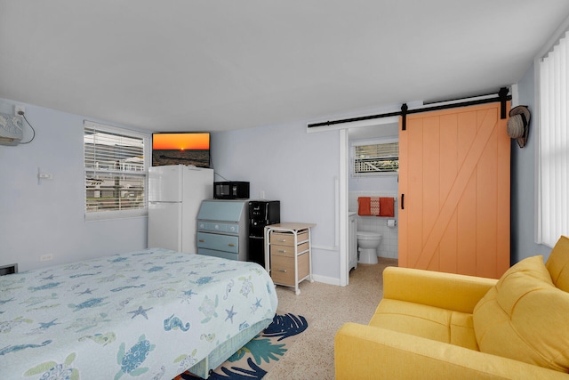 bedroom featuring white refrigerator, a barn door, and ensuite bath