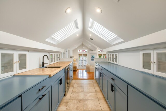 kitchen with sink, light tile patterned floors, dishwasher, butcher block counters, and vaulted ceiling with skylight