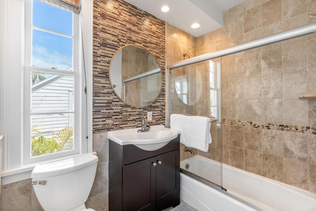 full bathroom featuring toilet, tasteful backsplash, bath / shower combo with glass door, tile walls, and vanity