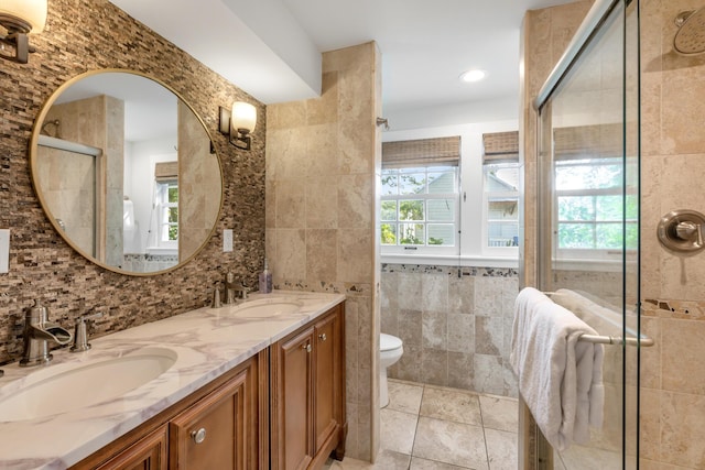 bathroom with a shower with door, vanity, tile walls, and toilet