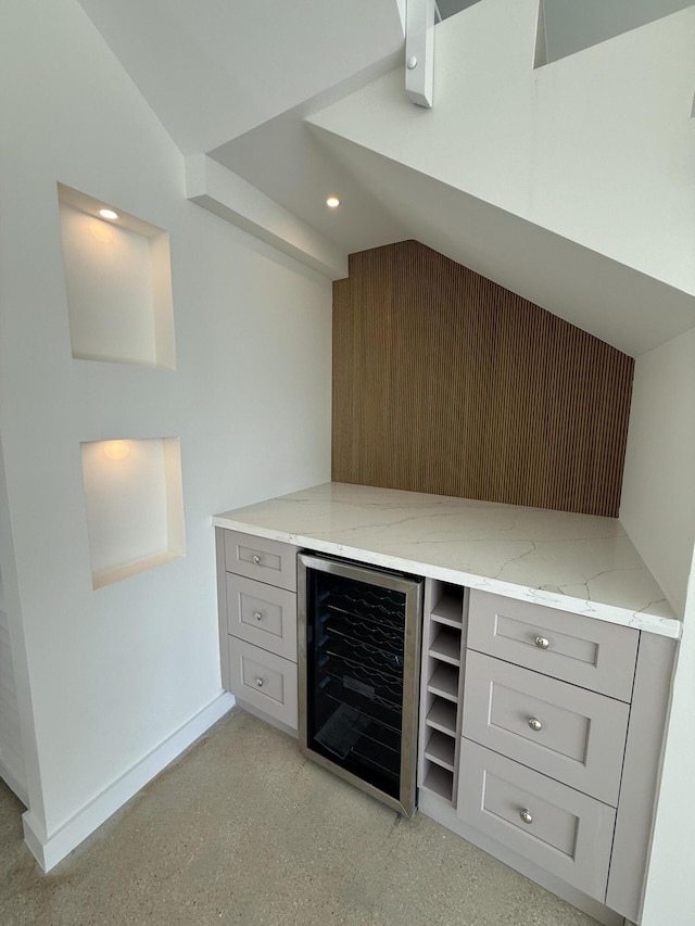 bar with lofted ceiling, gray cabinets, light stone countertops, and beverage cooler