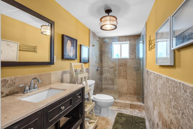 bathroom with tiled shower, vanity, toilet, and tile walls