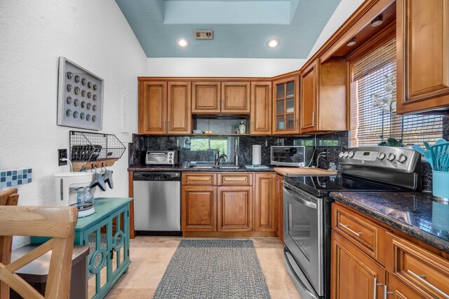 kitchen with sink, backsplash, stainless steel appliances, and dark stone counters