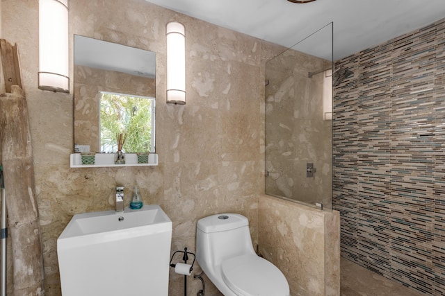 bathroom featuring tiled shower, toilet, and tile walls