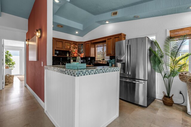 kitchen featuring a wealth of natural light, stainless steel fridge, kitchen peninsula, and vaulted ceiling