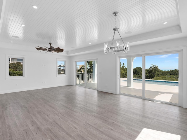 unfurnished living room featuring ceiling fan with notable chandelier, a tray ceiling, light hardwood / wood-style floors, and wooden ceiling