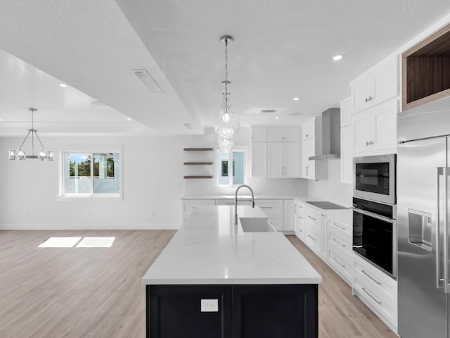 kitchen with sink, hanging light fixtures, a large island, built in appliances, and wall chimney range hood