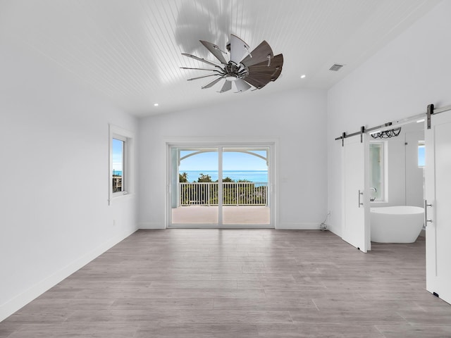 unfurnished room with light hardwood / wood-style flooring, a barn door, ceiling fan, and vaulted ceiling