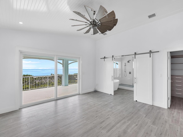 unfurnished living room with a wealth of natural light, a barn door, ceiling fan, and light wood-type flooring