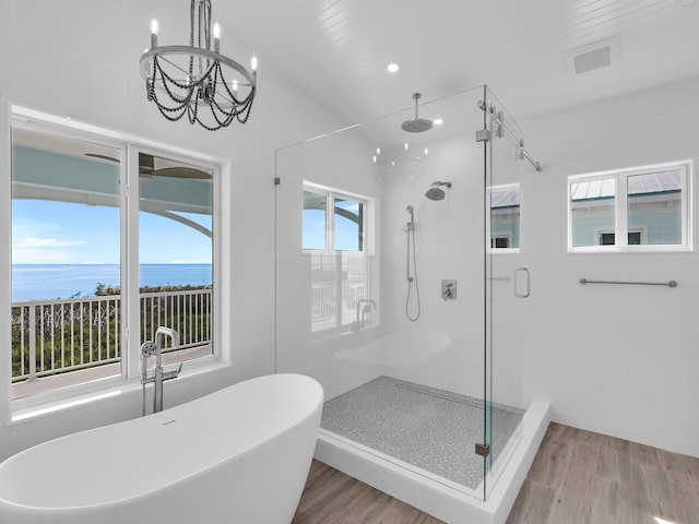 bathroom with hardwood / wood-style floors, independent shower and bath, tile walls, a chandelier, and a water view