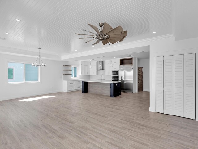 unfurnished living room with ceiling fan with notable chandelier, crown molding, sink, and light wood-type flooring