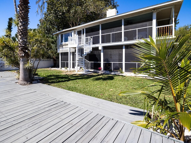 back of property featuring a wooden deck, a yard, and a sunroom