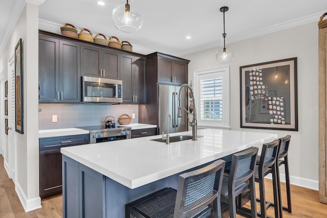 kitchen with dark brown cabinetry, sink, decorative light fixtures, stainless steel appliances, and a kitchen island with sink