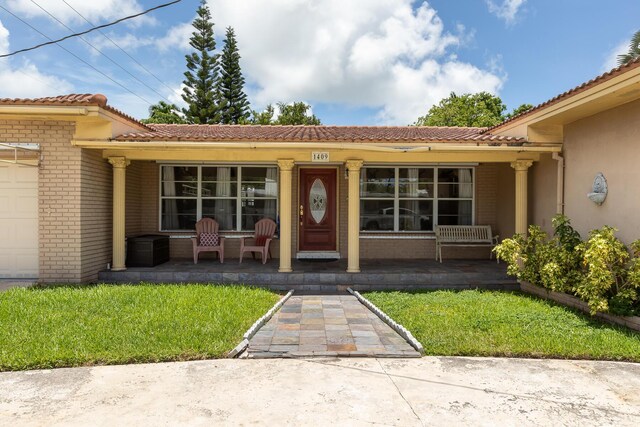 view of exterior entry featuring a garage, covered porch, and a lawn