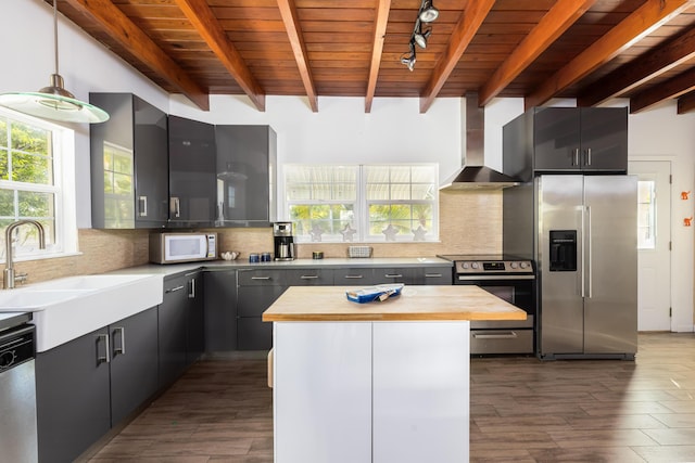 kitchen featuring appliances with stainless steel finishes, butcher block countertops, decorative light fixtures, a center island, and wall chimney exhaust hood