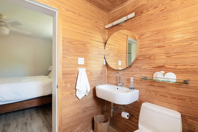 bathroom with sink, hardwood / wood-style flooring, ceiling fan, toilet, and wood walls