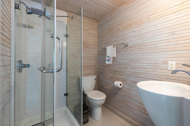 bathroom featuring sink, wooden walls, a shower with door, and toilet