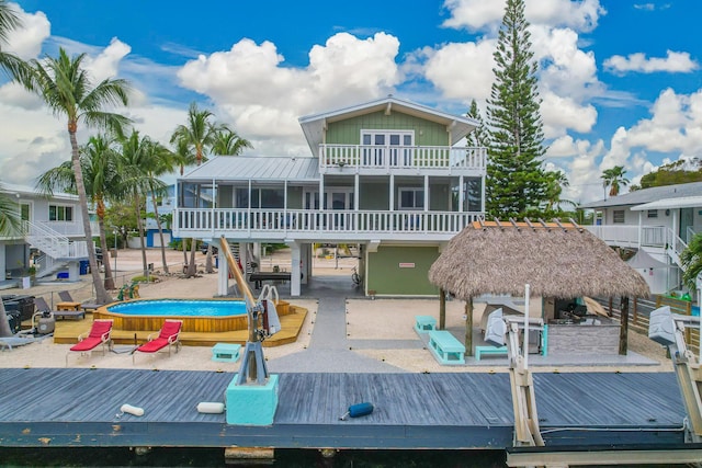 rear view of property featuring a pool, a sunroom, metal roof, a balcony, and stairs