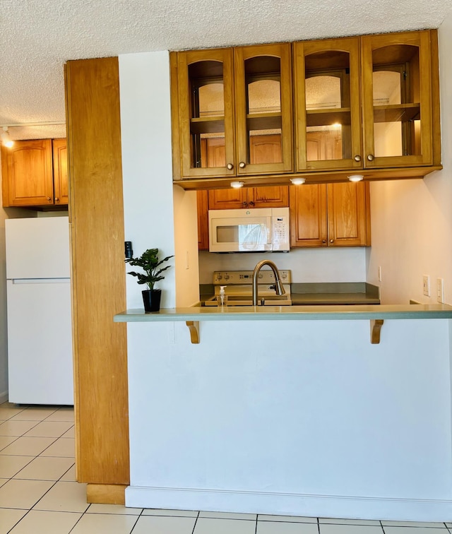 kitchen featuring light tile patterned flooring, a kitchen bar, a textured ceiling, kitchen peninsula, and white appliances