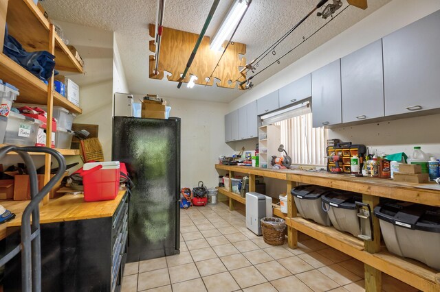 kitchen with black refrigerator, wooden counters, light tile patterned flooring, and a textured ceiling