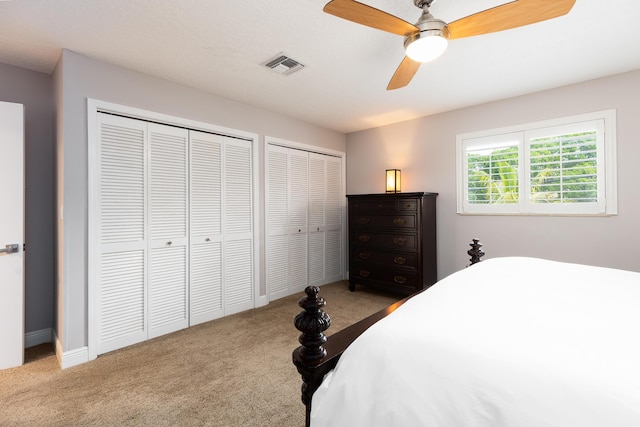 bedroom with two closets, light carpet, and ceiling fan