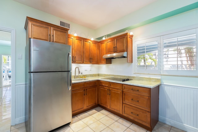 kitchen with sink, light tile patterned floors, stainless steel fridge, black electric stovetop, and light stone countertops