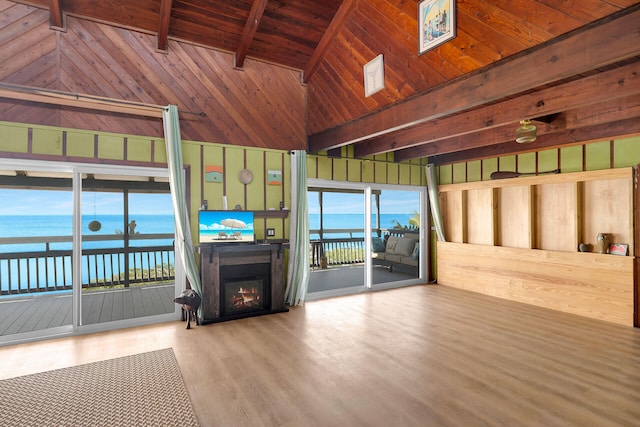 unfurnished living room with vaulted ceiling with beams, a wealth of natural light, wood walls, and a water view