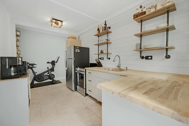 kitchen featuring stainless steel appliances, wood walls, a sink, white cabinetry, and open shelves